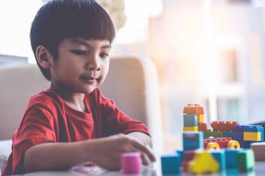 Asyalı çocuk oturma odasındaki masaya oyuncak blokları diziyor.