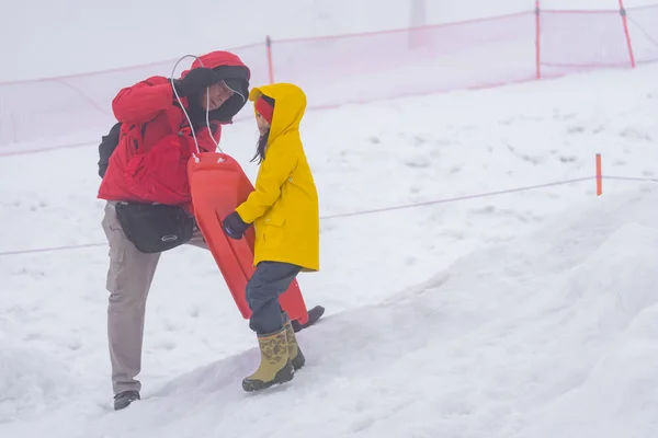 Father is helping her daughter to ride the snow sled — Stock Photo, Image