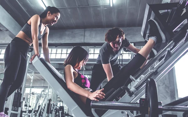 La mujer está trabajando en una máquina de pierna con entrenador masculino junto a la t. — Foto de Stock