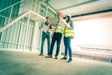 Üç mühendis erkek ve kadın bir inşaat alanındaki belge ve bilgisayarda tartışıyorlar..