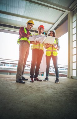 Üç mühendis erkek ve kadın bir inşaat alanındaki belge ve bilgisayarda tartışıyorlar..