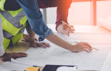 İnşaat mühendisi ve mimar inşaat planıyla birlikte çalışma masasında beyin fırtınası yapıyor.