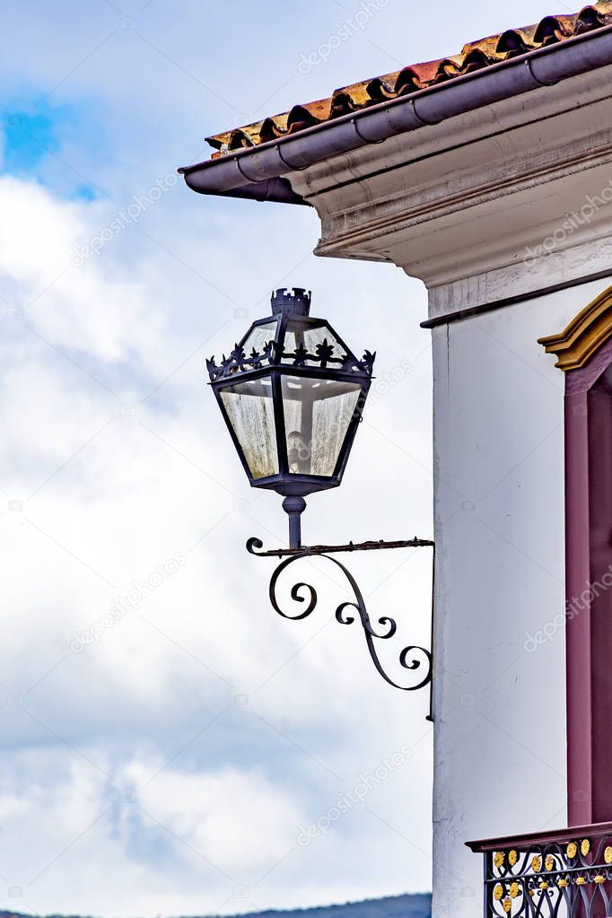 Old residential lighting lantern next to a window of an old colonial architecture building in the city of Ouro Preto in Minas Gerais