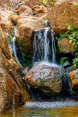 Kayalar ve tropik bitki örtüsü arasında akan suları olan küçük bir şelale.