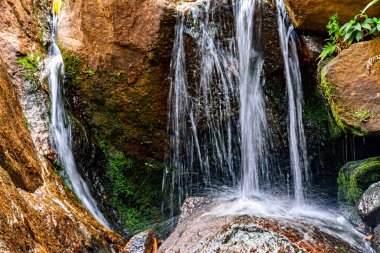 Kayalar ve bitki örtüsü arasında akan suları olan küçük bir şelale.
