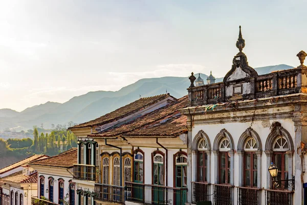 Ouro Preto şehrinin eski bir caddesinde, arka planda dağlarla birlikte koloni mimarisinde yüzler.