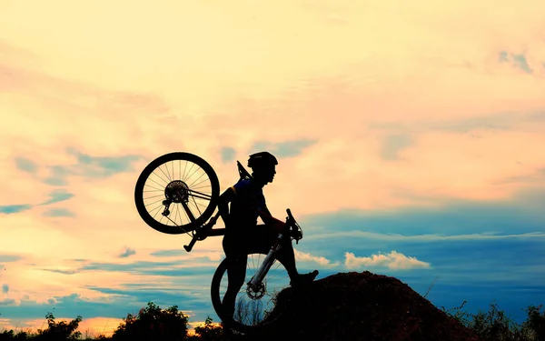 骑单车骑自行车的人在山顶上的草地上日落时的剪影迎接胜利的挑战 — 图库照片