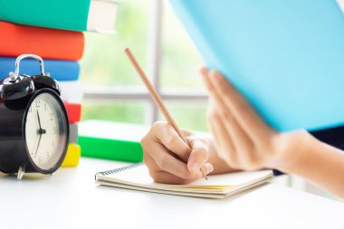 Adamın eli kağıt defter üzerine kalem tutuyor. Masanın üzerinde. Rahat pozisyonda.