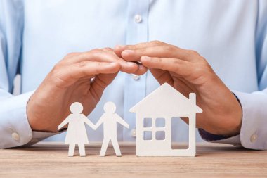 Bir genç aile ve ev sigorta. Tişörtlü adam iki erkek ve kadın ve ev iki elleriyle kapsar