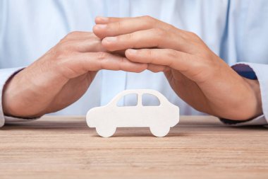 Car insurance. Man in a shirt covers his hand with a car clipart