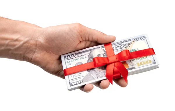 Έννοια, χρήματα ως δώρο, νίκη ή μπόνους. Χέρι του άνδρα λαμβάνει ή δίνει σωρό των 100 δολαρίων νομοσχέδια δεμένα με κόκκινη κορδέλα με φιόγκο. Απομονωμένα σε λευκό φόντο. — Φωτογραφία Αρχείου