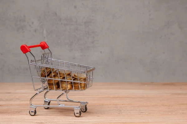 Shopping cart with coins on  wooden table — Stock Photo, Image