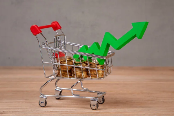 Shopping cart full of coins and  green arrow up — Stock Photo, Image