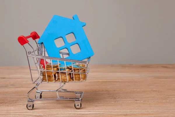 Venda ou comprar casa. Carrinho de compras com moedas e o símbolo da casa — Fotografia de Stock