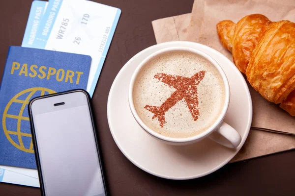 Mug of coffee with an airplane on the foam. Morning coffee with croissant in flight. Paspor and ticket with smrtrfonom — Stock Photo, Image