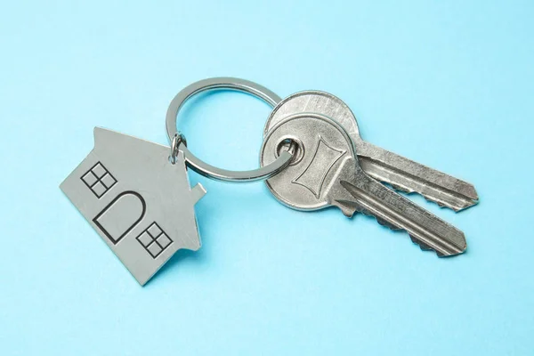 Ключі і будинок з брелоками на синьому фоні. Концепція купівлі будинку, оренда — стокове фото