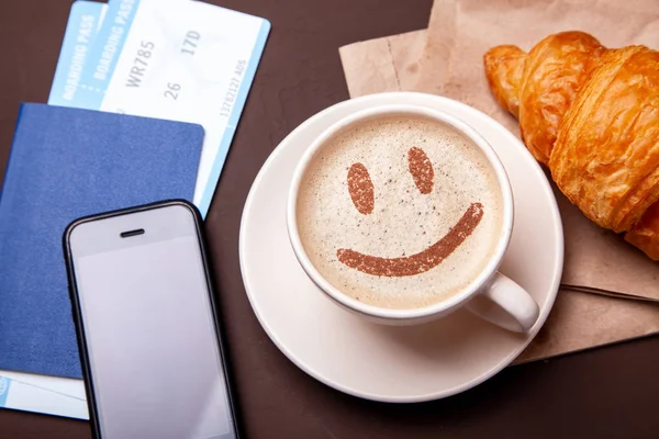 Pausa caffe ', caffe' mattutino. Tazza di caffè con schiuma e croissant con passaporto e biglietto aereo — Foto Stock