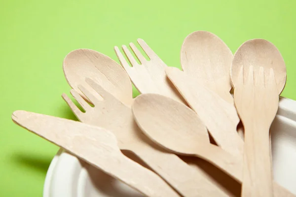 Eco-friendly disposable utensils made of bamboo wood and paper on a green. Draped spoons, fork, knives, bamboo bowls
