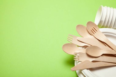Çevre dostu tek kullanımlık mutfak eşyaları bambu ahşap ve kağıt yeşil bir arka plan üzerinde yapılmış. Bol dökümlü kaşık, çatal, bıçak, kaseler ile bardak