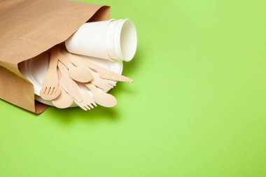 Çevre dostu tek kullanımlık mutfak eşyaları bambu ahşap ve kağıt yeşil bir arka plan üzerinde yapılmış. Bol dökümlü kaşık, çatal, bıçak, kaseler ile bardak