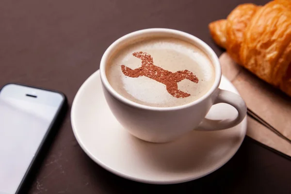 Tazza di caffè con chiave inglese sulla schiuma. Mi piace una pausa caffè con il croissant. Concetto di riparazione. sostegno — Foto Stock