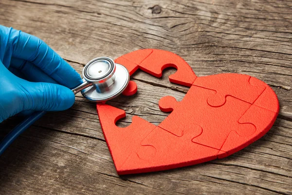 Coração enigma vermelho e estetoscópio em fundo de madeira. Conceito diagnóstico e tratamento de doenças cardíacas, seguro médico — Fotografia de Stock