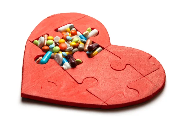 Hjärtat pussel röd och färgade piller och kapslar isolerad på vit bakgrund. Begreppet behandling av hjärtsjukdomar piller — Stockfoto