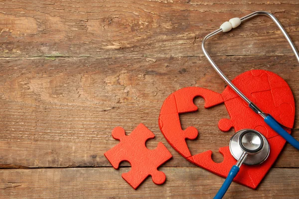 Cuore puzzle rosso e stetoscopio su sfondo di legno. Concetto diagnosi e trattamento delle malattie cardiache, assicurazione medica — Foto Stock