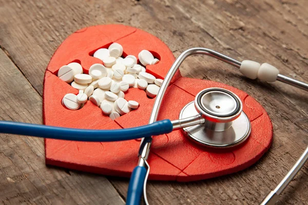 Serce puzzle, białe i czerwone pigułki i stetoskop na podłoże drewniane tła. Koncepcja leczenia chorób serca pigułki — Zdjęcie stockowe