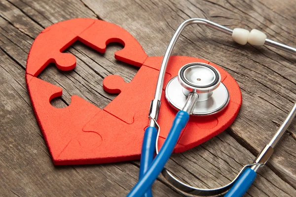 Cuore puzzle rosso e stetoscopio su sfondo di legno. Concetto diagnosi e trattamento delle malattie cardiache, assicurazione medica — Foto Stock