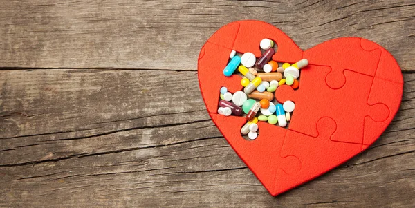 Serce puzzle czerwone i kolorowe tabletki i kapsułki na tle drewna. Koncepcja leczenia chorób serca pigułki. Kopiować miejsca na tekst — Zdjęcie stockowe