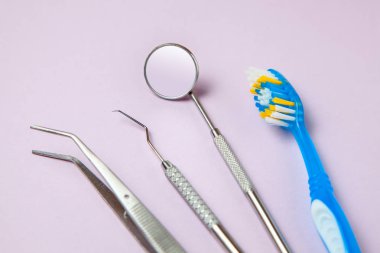 Diş fırçası ve diş araçları ayna, kanca ve cımbız mor zemin üzerine. Diş Bakımı ve diş hekimi ziyareti