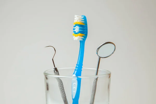 Toothbrush blue and dental tools mirror and hook in glass. Dental care and visit to dentist — Stock Photo, Image