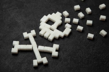 Siyah arka plan üzerinde beyaz şeker küplerini kafatasından. Çok hızlı ulevodov vücut için zararlı ve şeker öldürür. Diyabet 