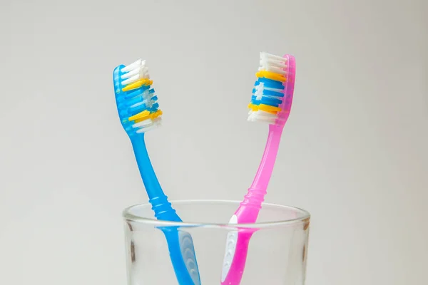 Two denture pink and blue in glass on gray background. The concept of toothbrushes for couple, joint residence — Stock Photo, Image