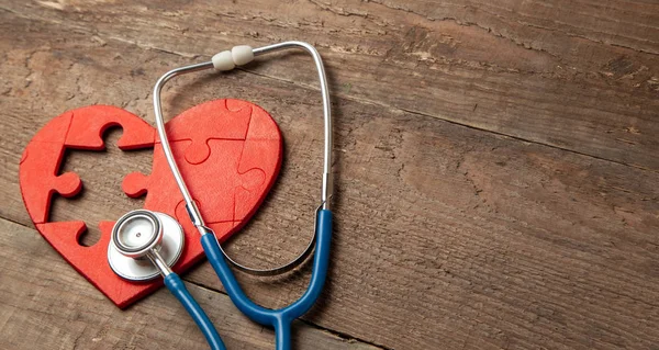 Cuore puzzle rosso e stetoscopio su sfondo di legno. Concetto diagnosi e trattamento delle malattie cardiache, assicurazione medica — Foto Stock