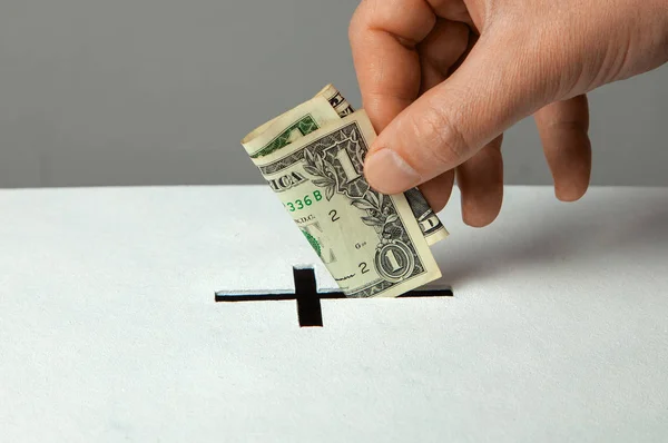 El hombre pone la donación en su mano con el dólar en la ranura en forma de cruz cristiana Imagen De Stock