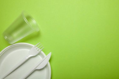 Yeşil zemin üzerine plastik tek kullanımlık kaplar. çatal, bıçak, tabak, bardak