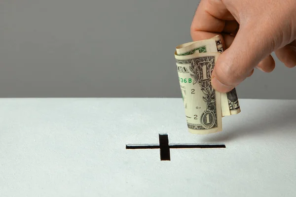 Man puts donation in his hand with dollar in slot in the form of Christian cross. Copy space for text — Stock Photo, Image