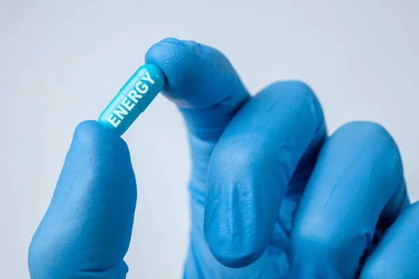 ENERGIA é escrito em cápsula pílula azul realizada nas mãos do médico em luvas. close-up — Fotografia de Stock