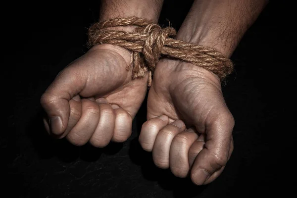Muž s rukama svázaný s lanem na černém pozadí. Pojem otroctví nebo vězeň. — Stock fotografie
