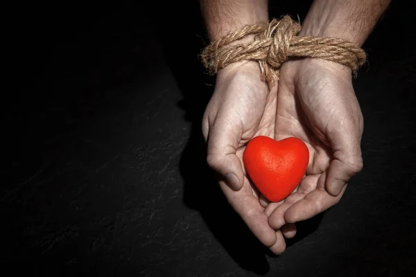 Man with hands tied rope and heart in his palms on black background. Love concept binds hands. Copy space for text.