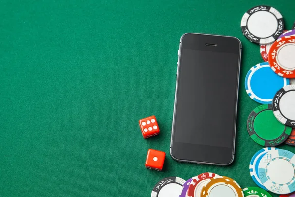 Mobile phone casino online. Mobile phone and dice chips on a green gaming table. Gambling addiction in cracking games