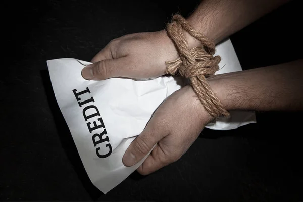 Credit limits financial opportunities. Man with his hands tied with rope is holding crumpled leaf with the inscription CREDIT — Stock Photo, Image