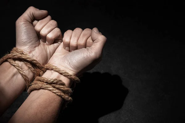 Man med händerna bundna med rep på svart bakgrund. Begreppet slaveri eller fånge. Kopiera utrymme för text. — Stockfoto