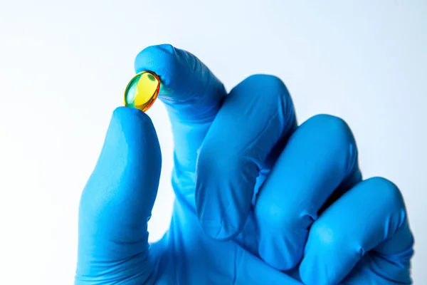 Comprimidos transparentes amarelos de óleo de peixe na mão do médico em luva azul . — Fotografia de Stock