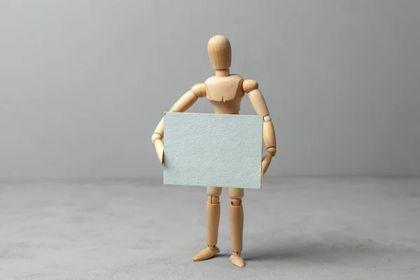 Wooden man holding blank board poster on gray background. — Stock Photo, Image