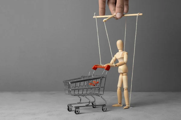 Контроль за поведением покупателя. Человек с тележкой из супермаркета, как кукла во главе с кукловодом. Копирование пространства — стоковое фото