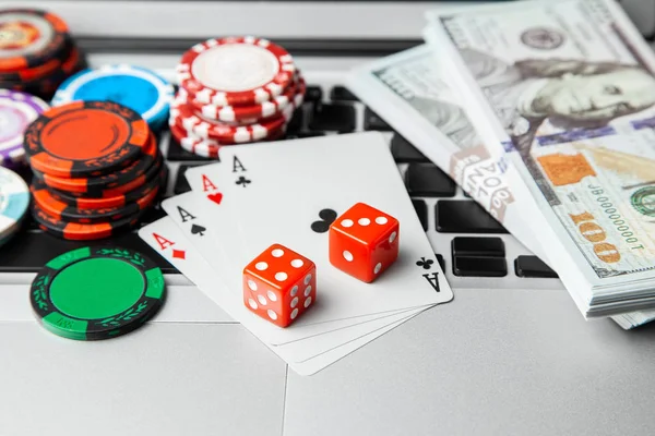 Online casino laptop. Laptop keyboard and chips with dice and playing cards and money cash dollars on green gaming table