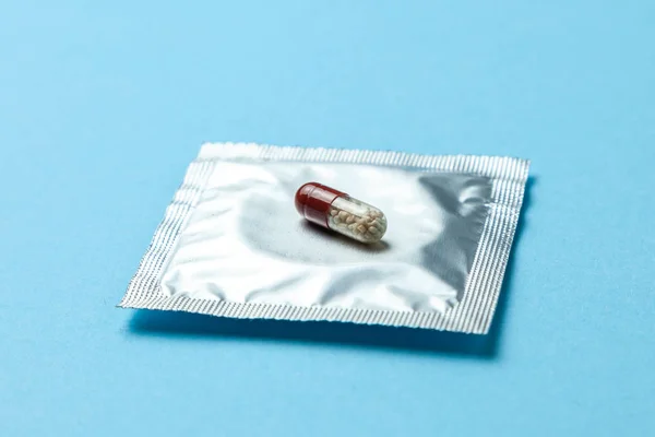 Pastillas anticonceptivas y preservativo en paquete en azul. El concepto de elegir el método anticonceptivo, píldoras anticonceptivas o condón — Foto de Stock